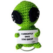 Front-facing Currently on a Side Quest green alien crochet critter with message